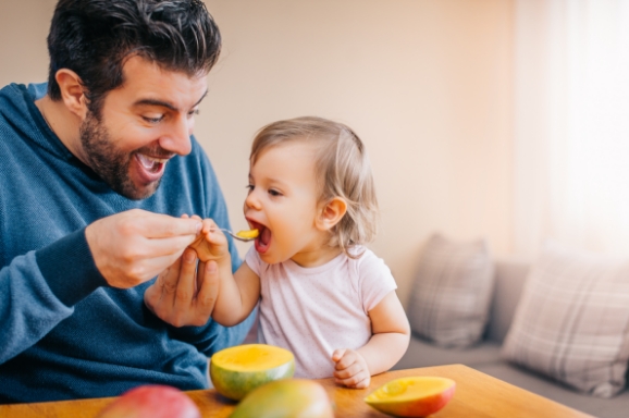 Dad feeding happy young child a spoon full of healthy food. 