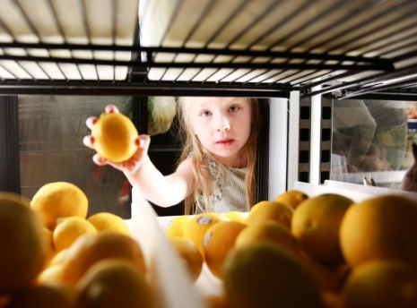 A young girl grabbing an orange at the food shelf. 
